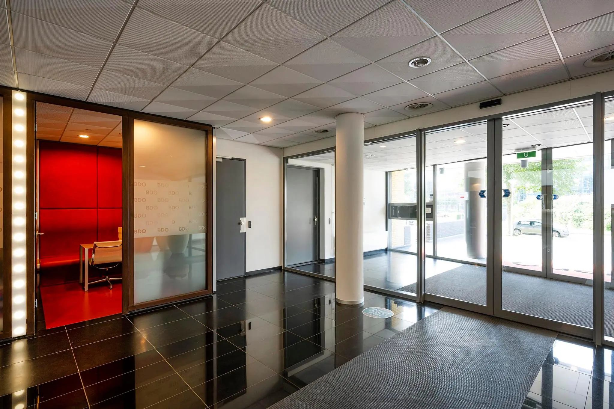 Ingangshal van het kantoorgebouw aan de K.P. van der Mandelelaan met glazen deuren, strakke zwarte vloertegels en zicht op een vergaderruimte van BDO.